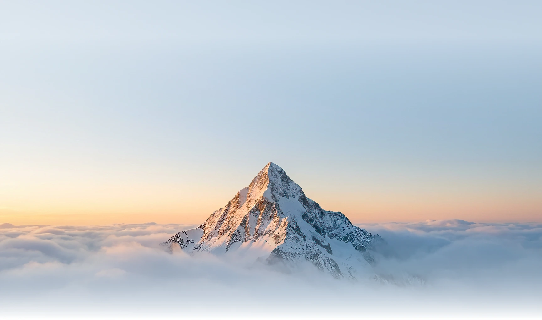 Bergspitze, die aus den Wolken herausragt mit hellblauem Himmel, der in orange übergeht.